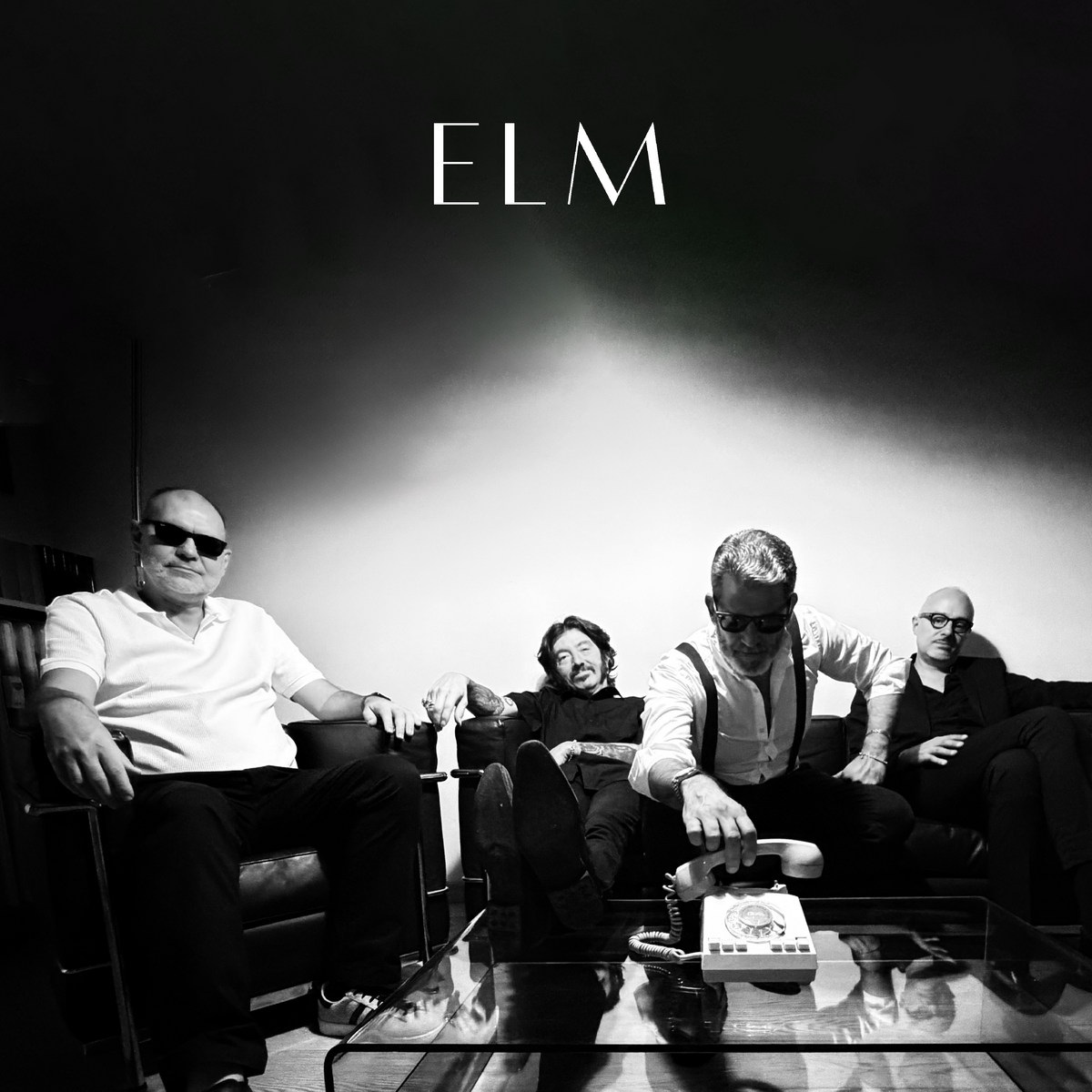 Die Band "ELM". Vier Männer sitzen auf einem Sofa, einer greift zu einem Telefon am Tisch vor sich. Darüber das Logo der Band.