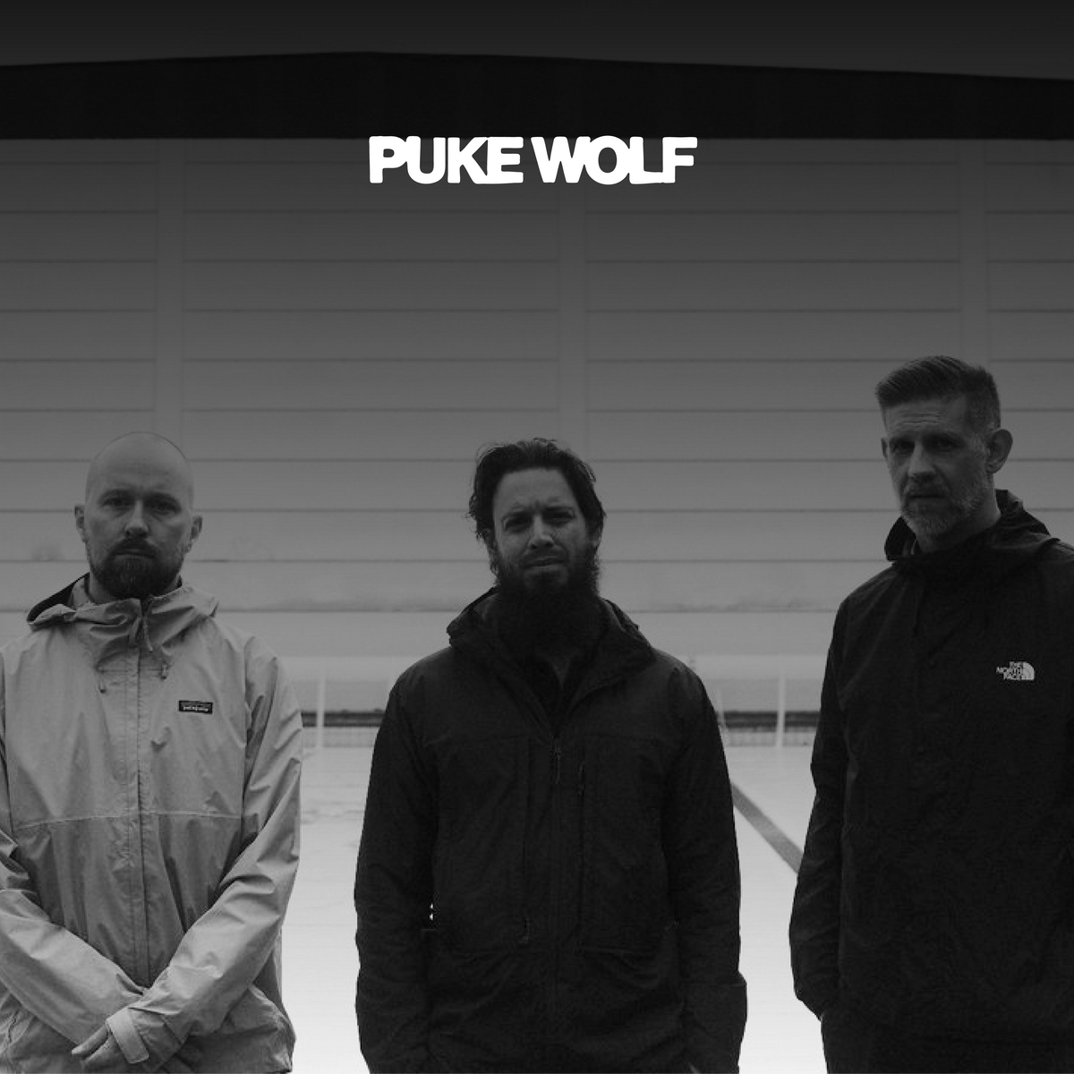 Die Band "Puke Wolf". Drei Männer stehen nebeneinander vor einem weißen Gebäude, blicken in die Kamera. Darüber in weiß das Logo der Band.