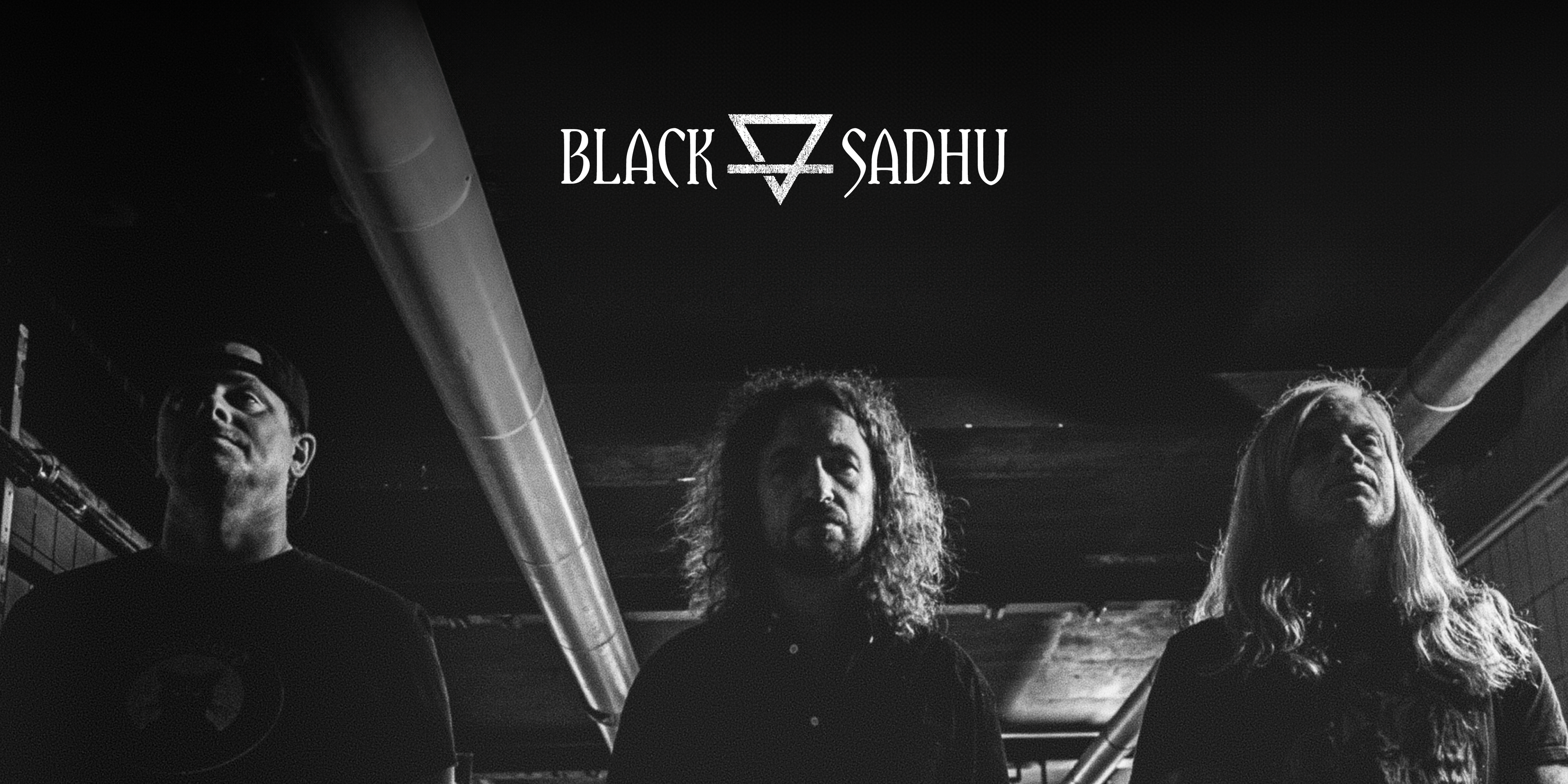 Die Band "Black Sadhu". Drei Personen in einer Tiefgarage oder einem Keller. Oben in der Mitte das Logo der Band.