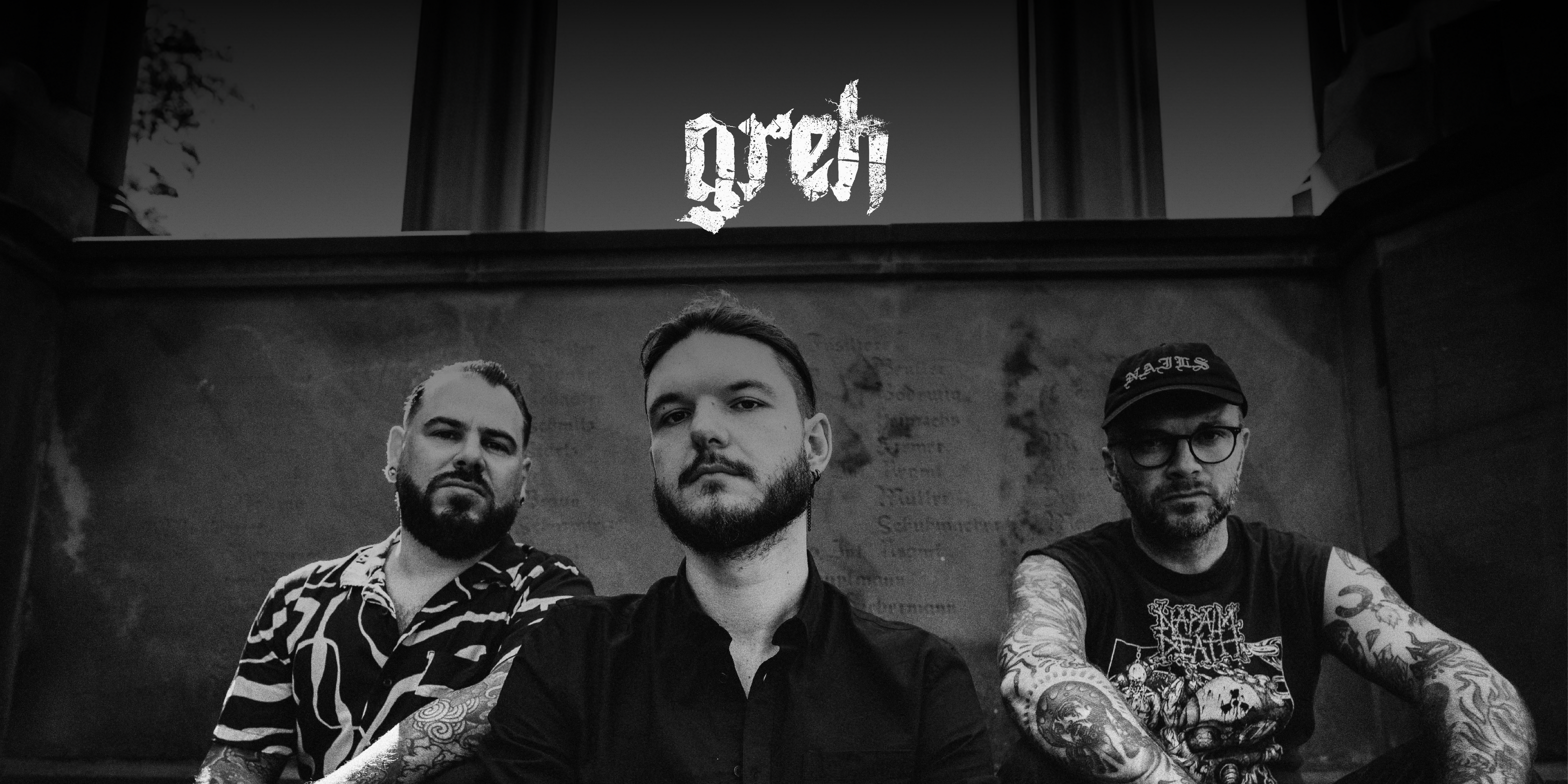 Die Band "greh". Drei Personen sitzen am Boden, blicken in die Kamera. Darüber das Logo der Band
