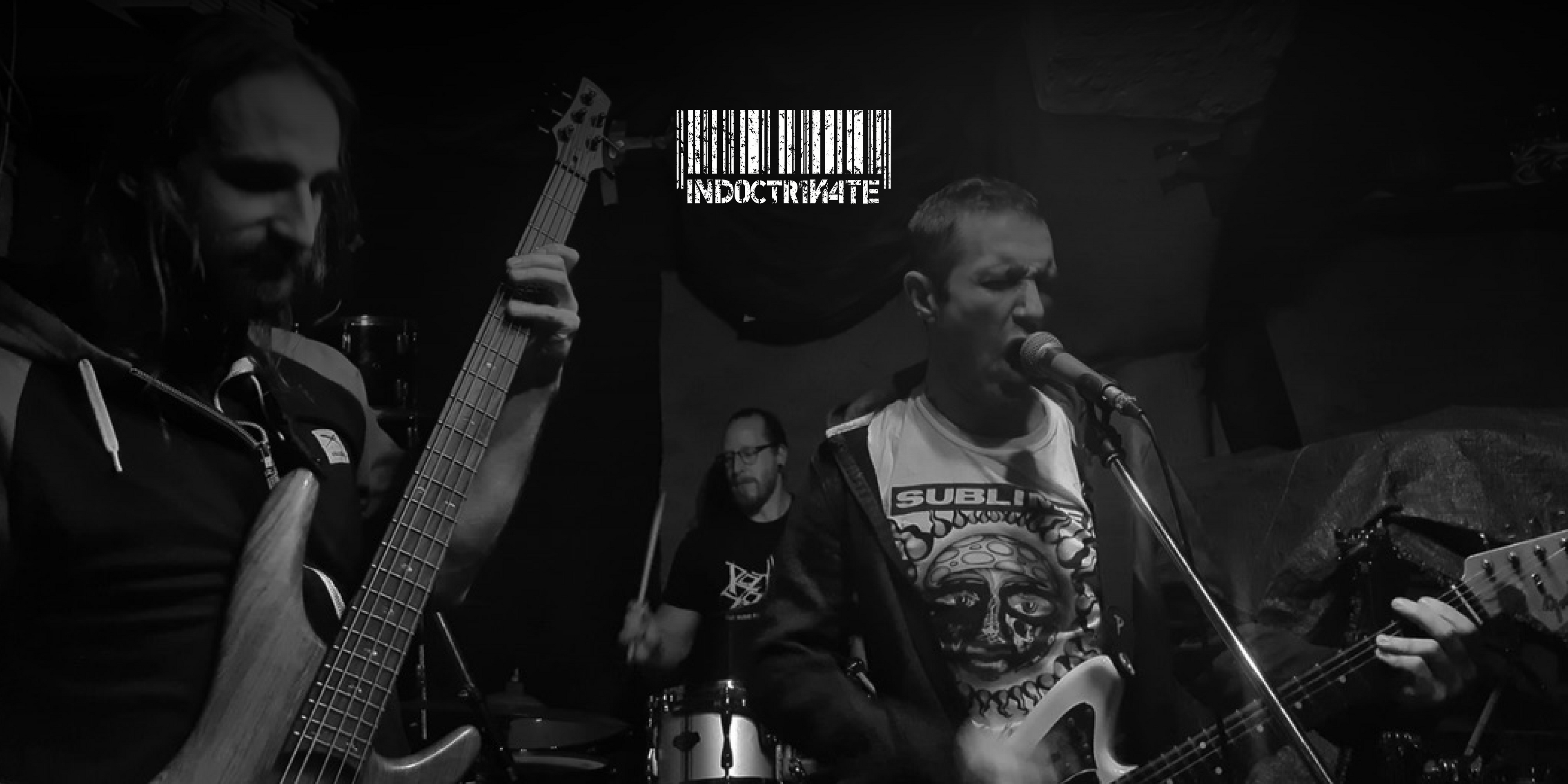 Die Band "Indoctrinate", währen sie musizieren. Oben in der Mitte das Logo der Band.