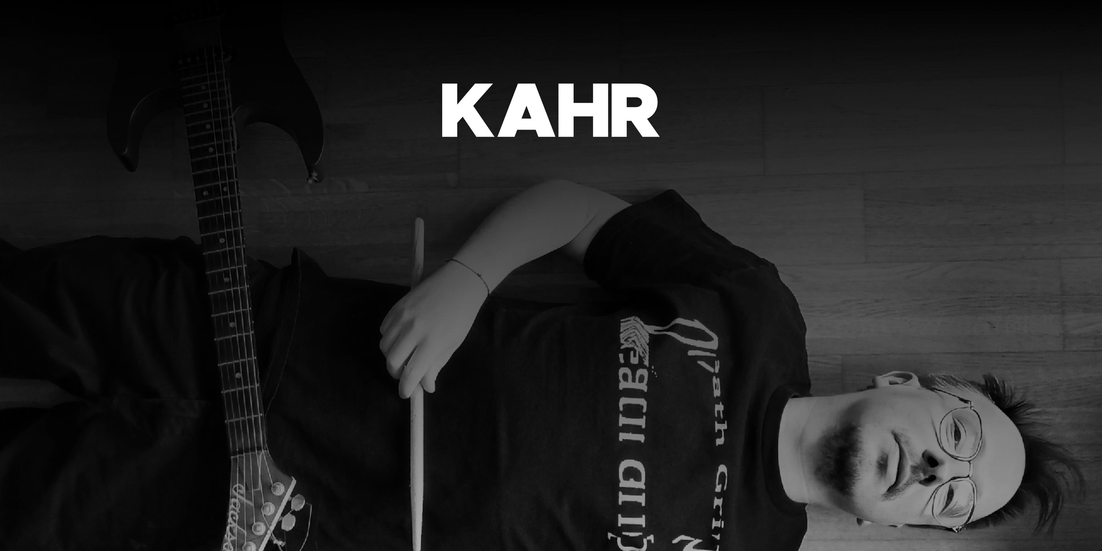 Der Musiker "KAHR", am Boden liegend, von oben fotografiert. Auf ihm liegt eine Gitarre, in der Hand hält der einen Drumstick. Oben in der Mitte das Logo. 
