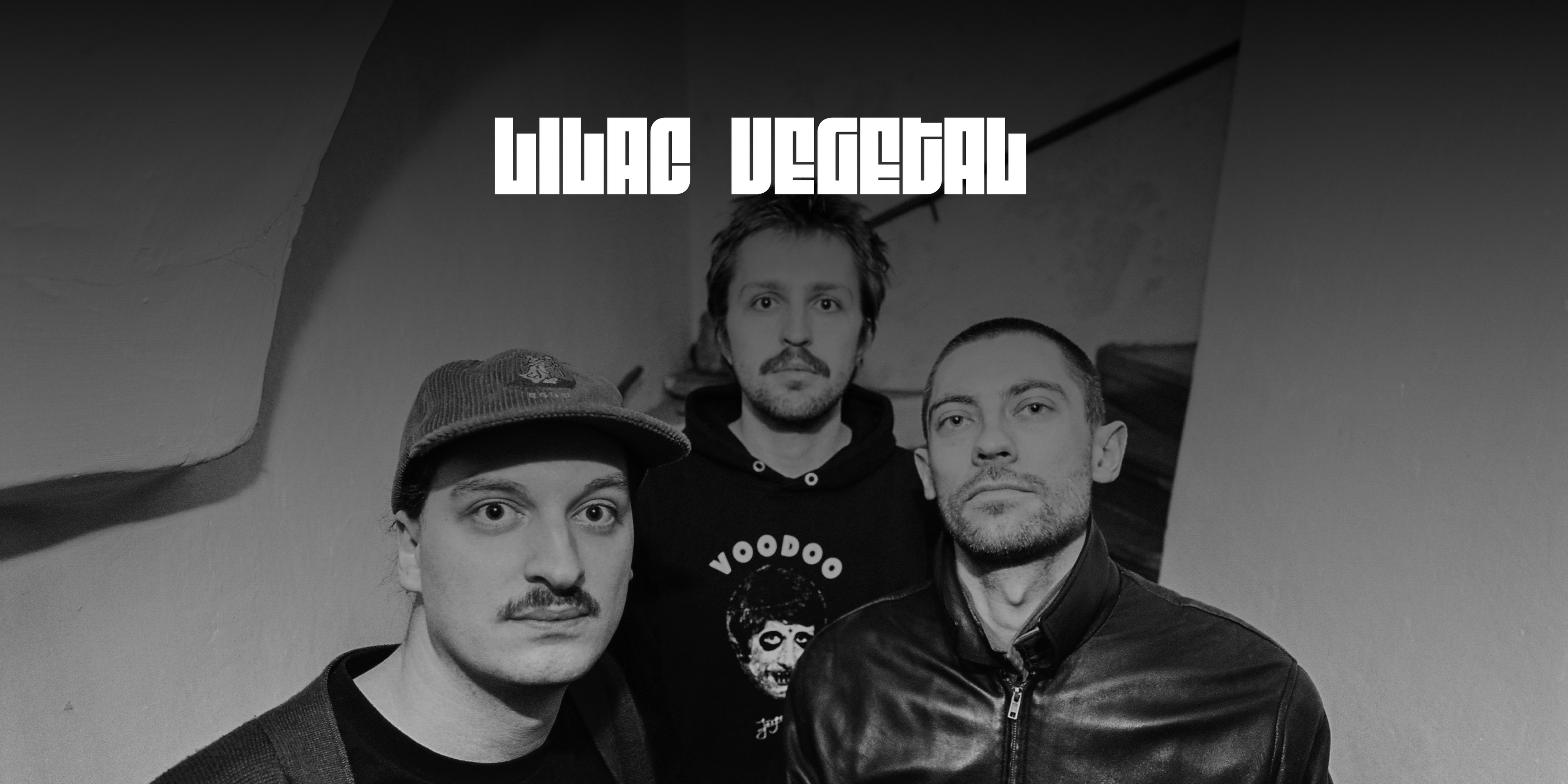 Die Band "Lilac Vegetal". Drei Personen in einem Stiegenhaus blicken in die Kamera. Oben in der Mitte das Logo der Band.