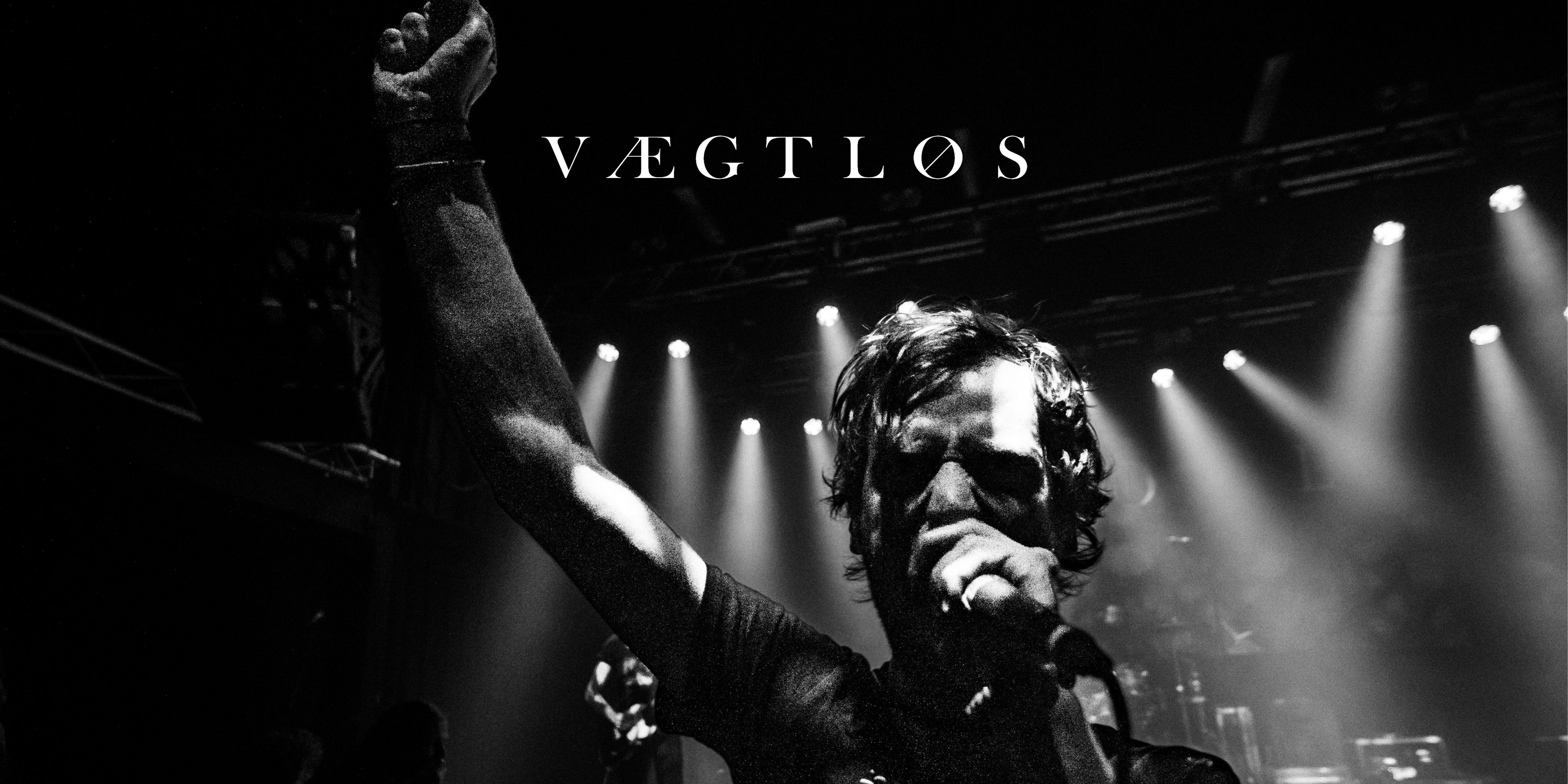 "Vægtløs" live. Eine Person in der Mitte mit Mikrofon, streckt eine Faust in die Luft. Darüber in der Mitte das Logo der Band.