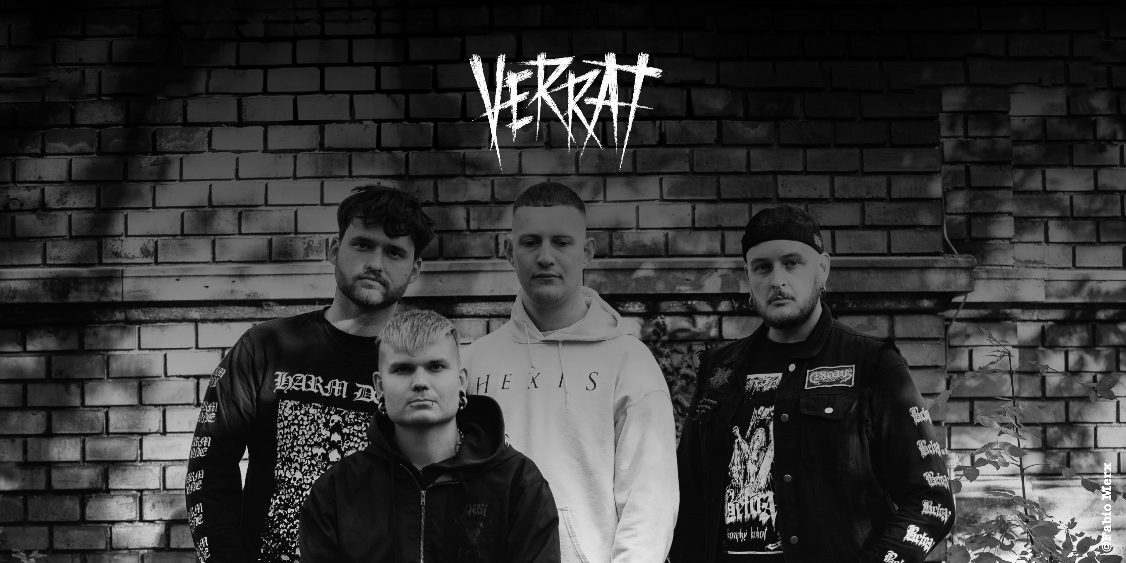 Die Band "Verrat". Vier Personen stehen/sitzen vor einer Maier, blicken teilweise in die Kamera.